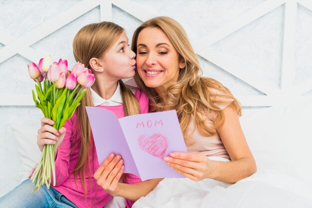 Figlia che bacia madre con biglietto di auguri