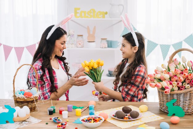 Figlia che dà i tulipani gialli del fiore a sua madre con la preparazione di giorno di pasqua a casa