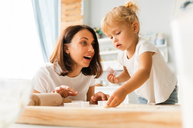 Figlia curiosa e madre felice che preparano i biscotti