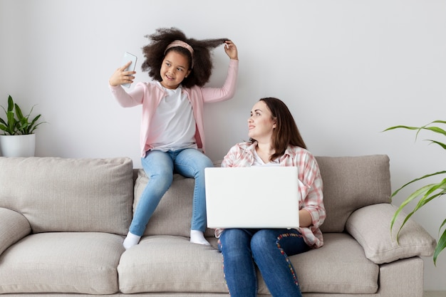 Figlia di vista frontale che prende un'immagine mentre la madre sta lavorando