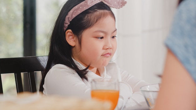 Figlia giapponese asiatica annoiata con alimento. Stile di vita bambini triste antipatia cibo pasto sconvolto colazione in cucina moderna a casa la mattina.