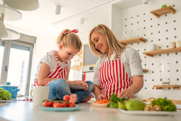 Figlia sveglia che gioca sul telefono mentre la madre sta cucinando