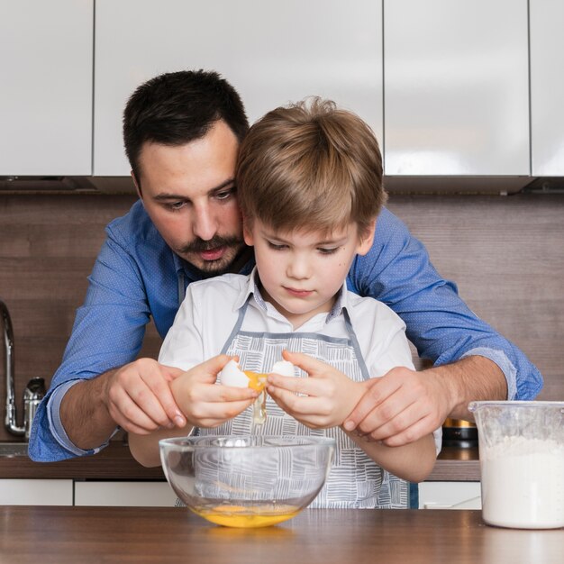 Figlio d'aiuto del padre di vista frontale per rompere le uova