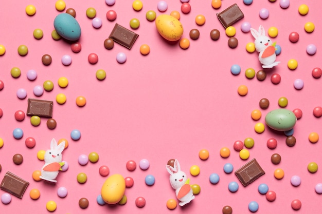 Figurina di coniglietto; caramelle di gemme; uova di Pasqua di cioccolato con spazio al centro su sfondo rosa