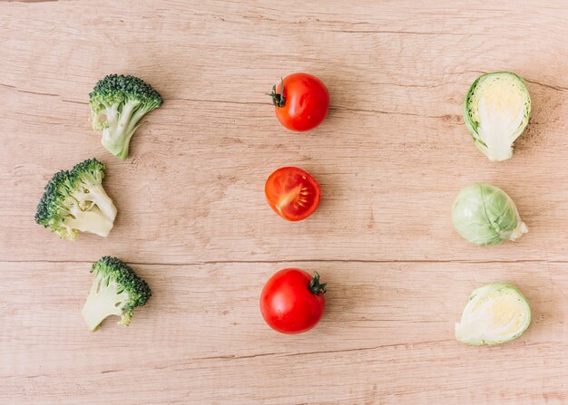 Fila di cavoletti di Bruxelles; broccoli e pomodorini sullo sfondo in legno