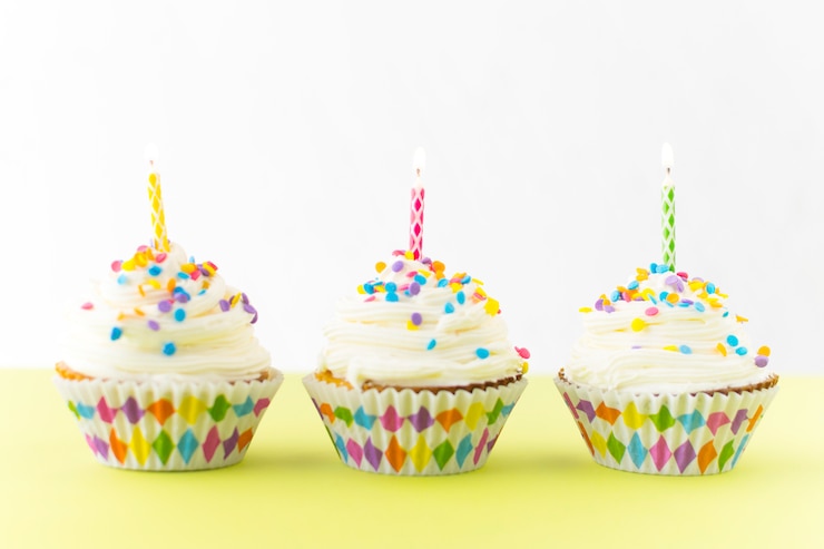 Foto gratuito fila di cupcakes freschi con candele colorate sulla superficie gialla
