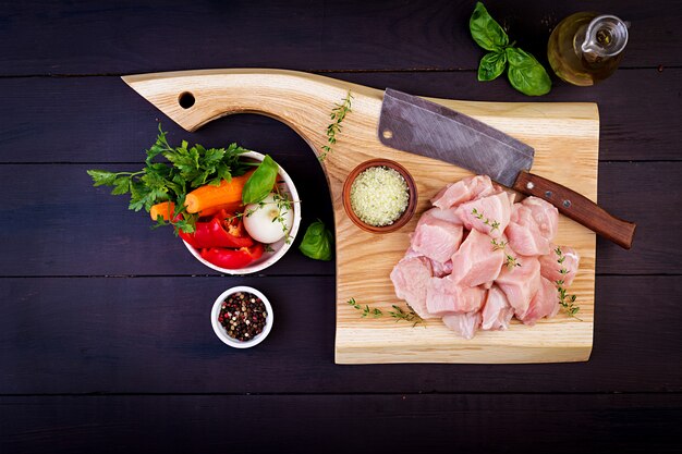 Filetti di petto di pollo crudo sul tagliere di legno con erbe e spezie. Vista dall'alto