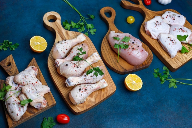 Filetto di carne di pollo crudo, coscia, ali e zampe con erbe, spezie, limone e aglio su sfondo blu scuro. Vista dall'alto