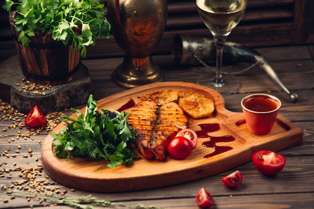 Filetto di pesce alla griglia con pomodoro, salsa rossa, erbe aromatiche e un bicchiere di vino bianco.