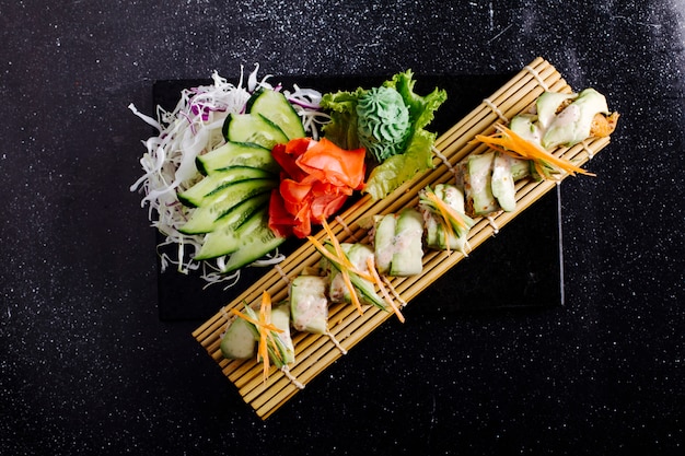 Filetto di pesce bianco sulla stuoia di sushi con zenzero, wasabi e cetriolo sulla tavola nera.