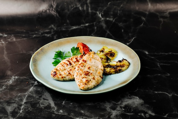 Filetto di pesce grigliato con melanzane e servito con pomodoro e prezzemolo.