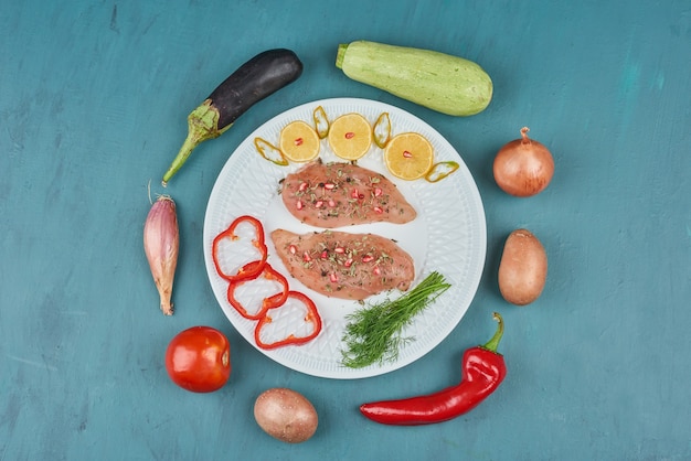 Filetto di pollo crudo in un piatto bianco con erbe e verdure.