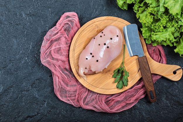 Filetto di pollo crudo su tavola di legno con verdure e coltello.