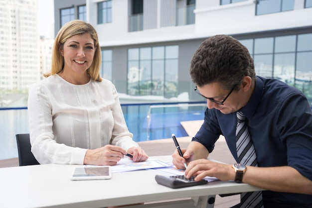 Finanziere femminile maturo emozionante allegro che sorride mentre ragioniere che per mezzo del calcolatore