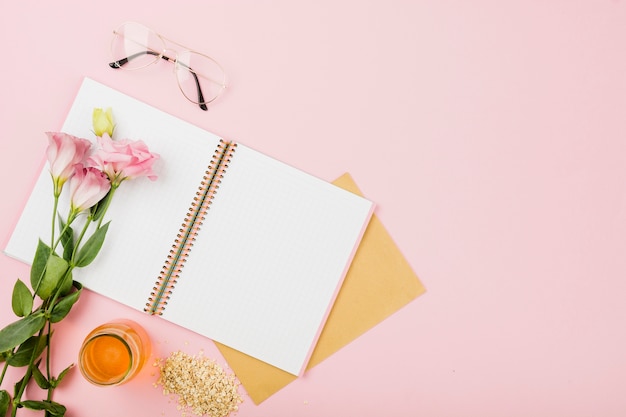 Fiore su un quaderno aperto; occhiali; barattolo di succo e muesli su sfondo rosa