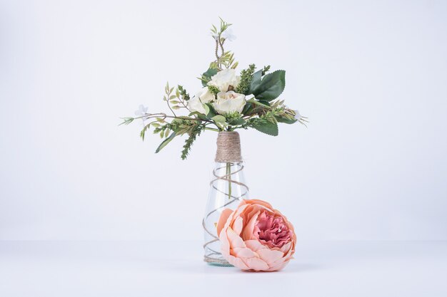 Fiori bianchi in vaso di vetro su bianco con rosa singola.