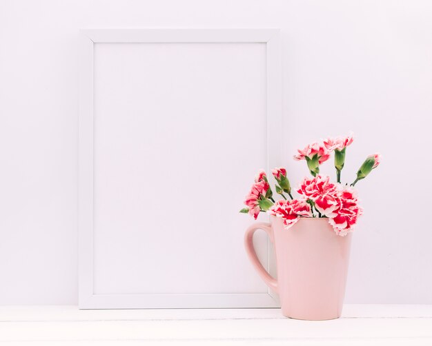 Fiori di garofano in vaso con cornice vuota sul tavolo