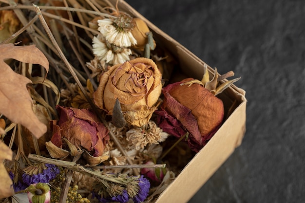 Fiori di rose essiccate con foglie secche in una scatola di carta.