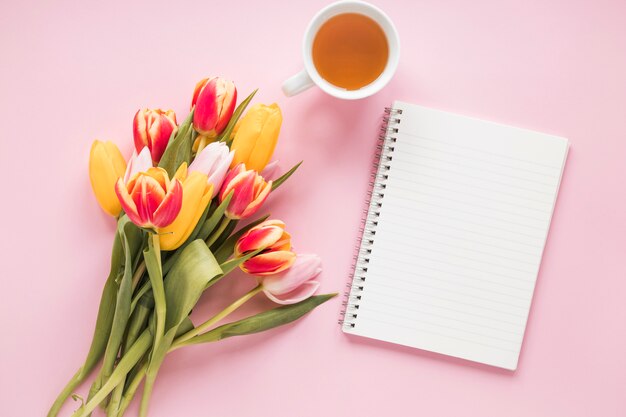 Fiori di tulipano con notebook e tazza di tè