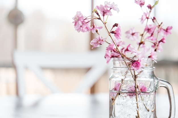 Fiori e rami di ciliegio in un bicchiere d'acqua sul tavolo sotto le luci