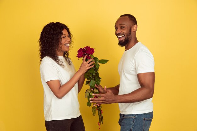 Fiori per il sorriso. Celebrazione di San Valentino, felice coppia afro-americana isolata su sfondo giallo studio. Concetto di emozioni umane, espressione facciale, amore, relazioni, vacanze romantiche.