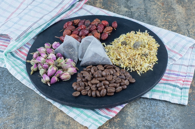 Fiori secchi, chicchi di caffè, cinorrodi e bustine di tè sul bordo nero.