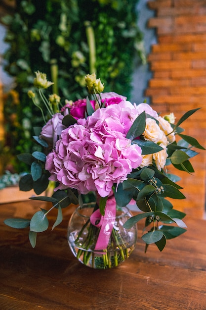 Fiorisca la composizione nella vista laterale delle rose arancio luminose delle ortensie del vaso di vetro