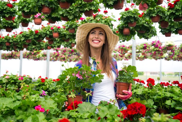 Fiorista abbastanza attraente della donna che lavora nel centro del giardino della serra che organizza i fiori in vaso per la vendita