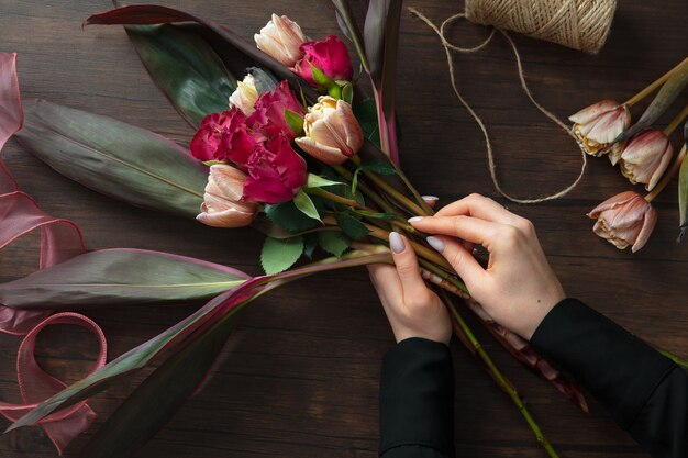 Fiorista al lavoro: donna che fa il bouquet moderno di moda di fiori diversi su una superficie di legno.