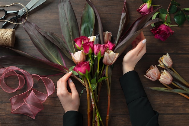 Fiorista al lavoro: donna che fa moda moderna bouquet di fiori diversi su una superficie di legno. Masterclass. Regalo per la sposa per il matrimonio, la festa della mamma, la festa della donna. Romantica moda primaverile. Rose della passione.