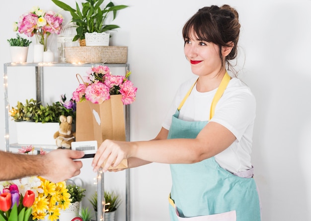 Fiorista femminile che dà il sacchetto di carta del fiore al suo cliente