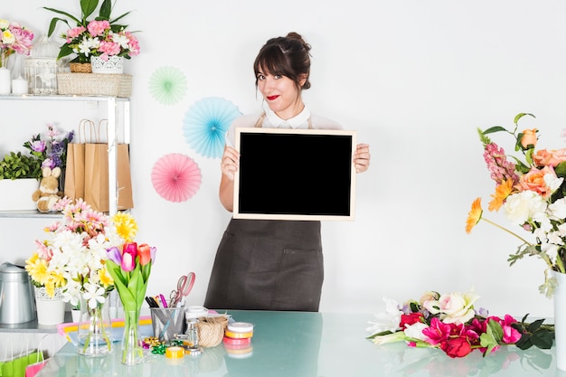 Fiorista femminile con l&#39;ardesia in bianco che esamina macchina fotografica