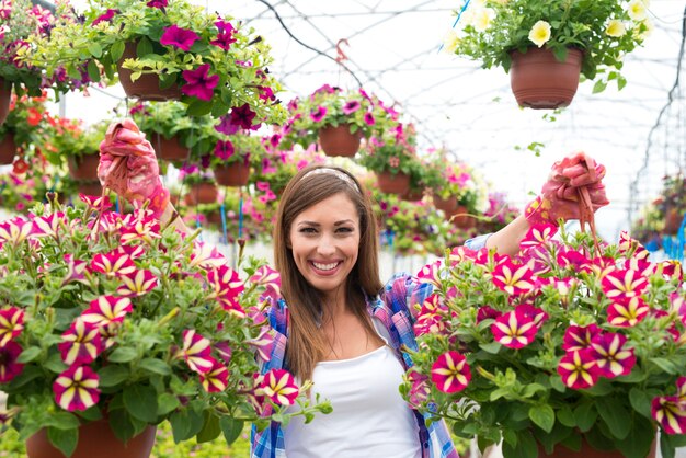 Fiorista femminile felice e sorridente che tiene la pianta del fiore del mazzo al centro del giardino della serra