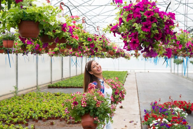 Fiorista sorridente felice che organizza i fiori e che gode del lavoro al giardino della serra