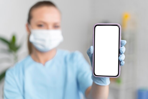 Fisioterapista femminile con mascherina medica che tiene smartphone