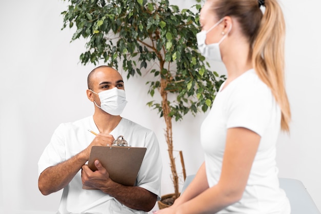 Fisioterapista maschio con maschera medica e donna che controlla appunti