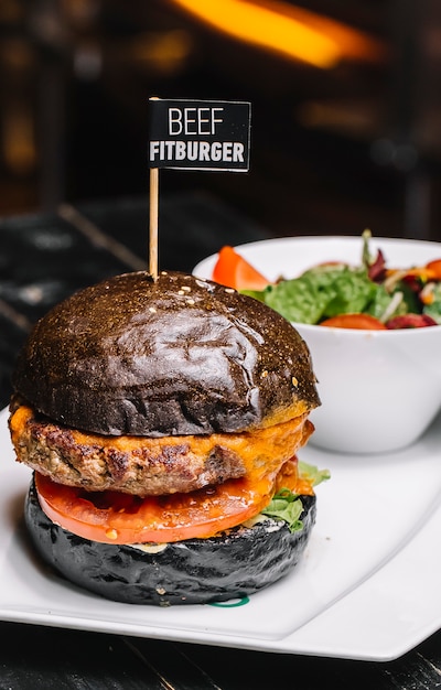 Fitburger di manzo vista laterale in un panino nero con insalata di verdure