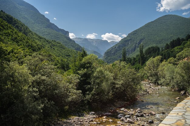 Fiume circondato da colline coperte di vegetazione sotto un cielo nuvoloso e luce solare