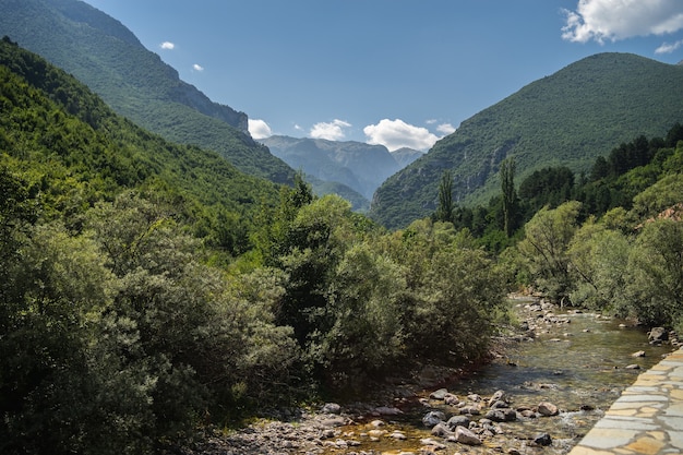 Fiume circondato da colline coperte di vegetazione sotto un cielo nuvoloso e luce solare