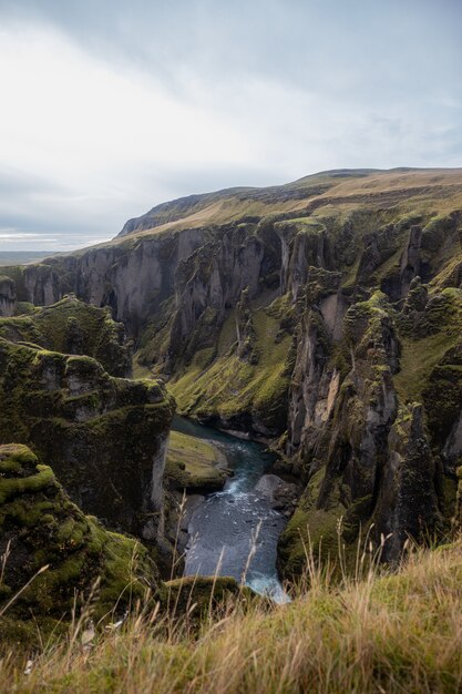 Fiume circondato da rocce coperte di vegetazione ed erba secca sotto un cielo nuvoloso