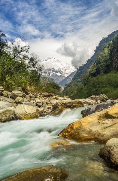 Fiume circondato da rocce ricoperte di verde e neve sotto un cielo nuvoloso