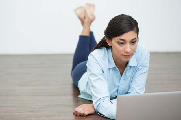 Focalizzata donna distesa sul pavimento e lavorare sul computer portatile