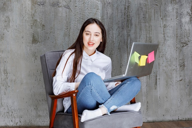 Focalizzato giovane donna seduta sulla poltrona che lavora al computer portatile. Foto di alta qualità