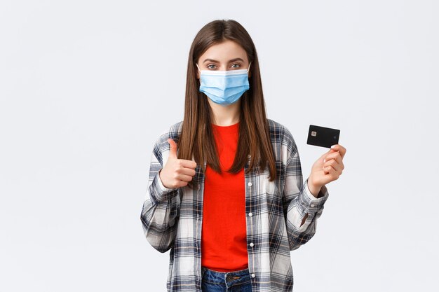 Focolaio di coronavirus, lavoro da casa, shopping online e concetto di pagamento senza contatto. La donna soddisfatta in maschera medica consiglia di utilizzare la carta di credito durante la pandemia, pollice in su