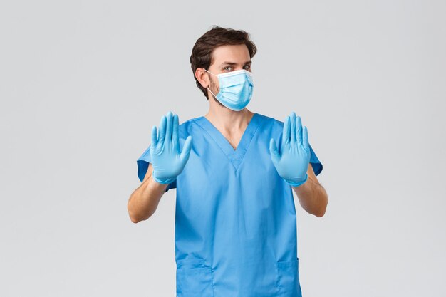 Focolaio di coronavirus, operatori sanitari che combattono malattie, concetto di ospedali. Medico riluttante e dispiaciuto in maschera medica, guanti e scrub, stop show, rifiutare o rifiutare l'offerta, agitando le mani