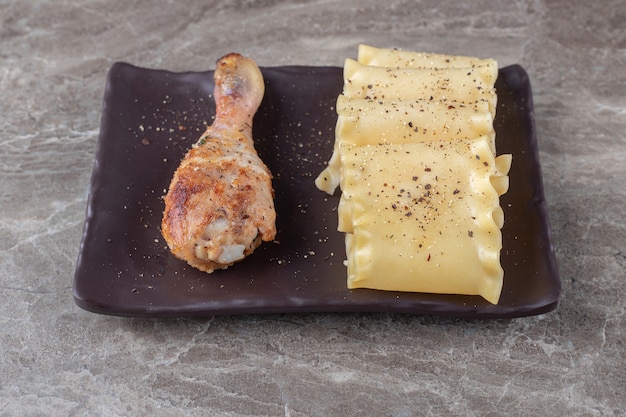 Fogli di lasagne piccanti accanto alla coscia di pollo sul piatto di legno, sul marmo.
