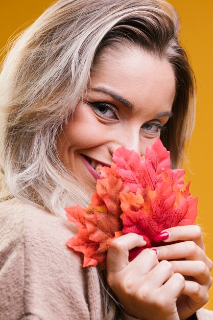 Foglie di acero graziose della tenuta della donna che esaminano macchina fotografica