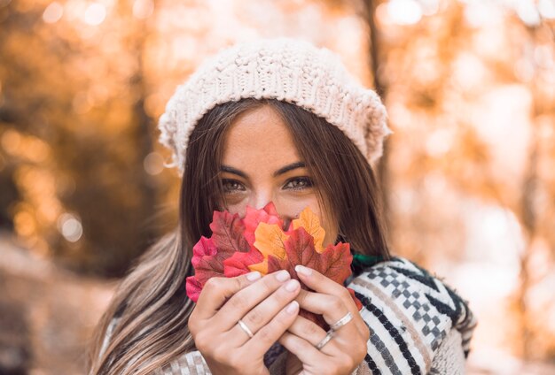 Foglie di autunno della tenuta della giovane donna vicino al fronte