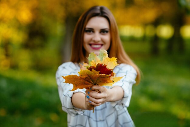 Foglie di autunno della tenuta della ragazza in entrambe le mani nel parco.