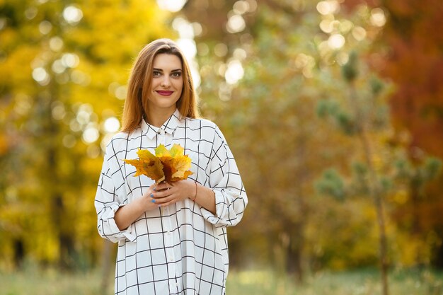 Foglie di autunno della tenuta della ragazza nel parco.